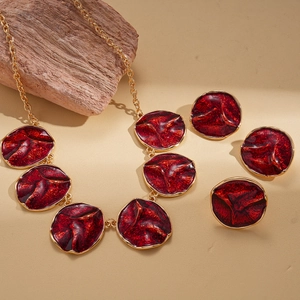 Vintage style red enamel gold necklace and earring jewelry set on textured beige surface