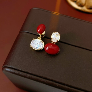 Dettaglio di orecchini vintage dorati con perline rosse e zirconi su pelle marrone