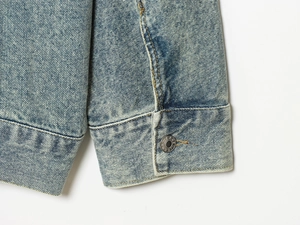 Macro shot of light blue denim jacket cuff with metal button and yellow stitching
