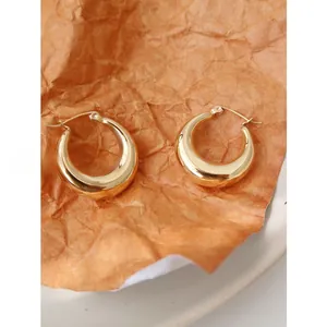 Detail of chunky gold hoop earrings with polished finish on textured paper