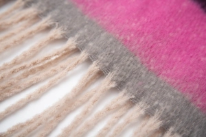 Close-up of thick knit striped scarf featuring soft pink and grey weave with fringe