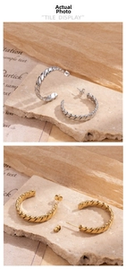 Detail of gold and silver C-shaped twisted rope earrings on a natural stone surface