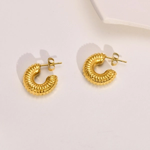 Detailed view of gold C-shape chunky hoop earrings with twisted texture on white background