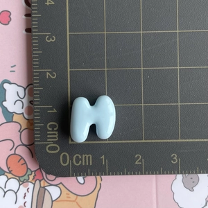 Macro detail of a 1.5cm light blue resin letter H accessory for DIY hair clips