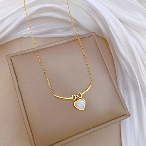 Close-up of golden bow-knot heart pendant with white mother of pearl inlay on chain