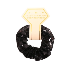 Close-up of black faceted sequin scrunchie on a decorative display card with gold text