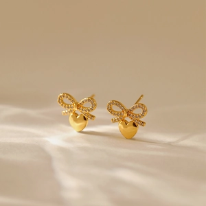 Gold bow heart earrings with sparkling crystals on elegant soft fabric background