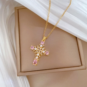 Titanium steel cross necklace with pink gemstone and pearls on a beige jewelry box