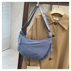 Detailed view of gray-blue nylon crescent crossbody bag hanging near a stylish trench coat