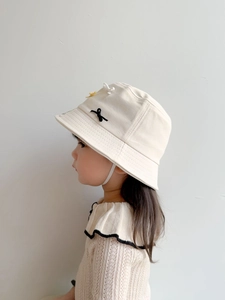 Detail of cream kids bucket hat featuring a black bow and small yellow flower accents
