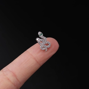 Macro shot of silver snake cartilage stud with white cubic zirconia and green eyes