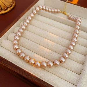 Close-up of pink pearl necklace with gold clasp in a beige velvet jewelry box