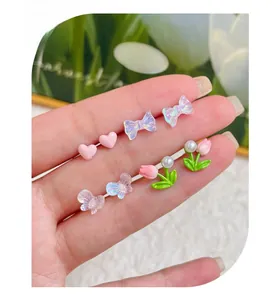 Detail of cute flower and butterfly earrings set held by hand for scale and texture