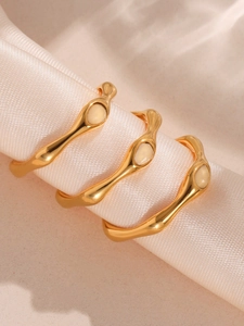 Detail of wave texture gold rings featuring oval gemstone on satin fabric