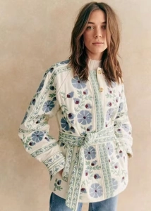 Détail de broderie florale sur une veste en coton blanche ceinturée à motifs bleus