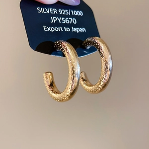 Macro shot of gold-plated C-shaped hoop earrings with hammered texture on black card