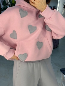Détail du sweat à capuche rose avec broderies de cœurs gris et poignets nervurés