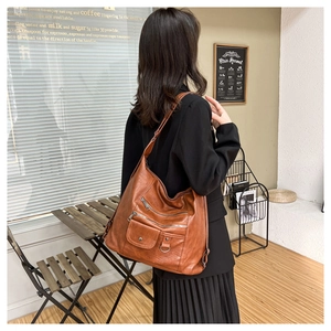 Detailed view of brown soft leather tote bag with multiple zip pockets on model's shoulder