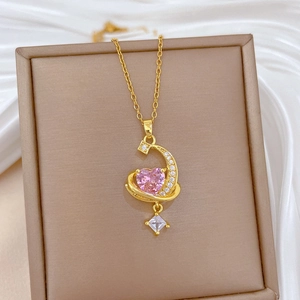 Macro detail of gold necklace with pink heart gem and crescent moon pendant on silk