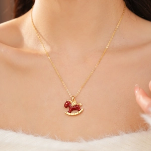 Detail of a golden necklace with red enamel rocking horse pendant on a female neck