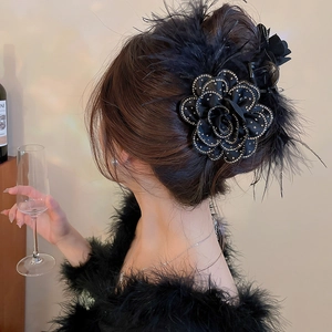 Close-up of elegant black fabric flower hair claw with feathers and rhinestone accents