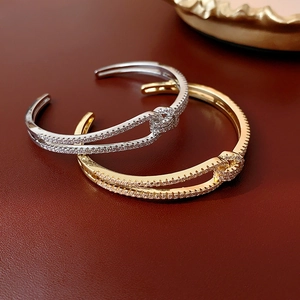 Detail of gold and silver knot bangles with zircon inlay on a dark leather surface