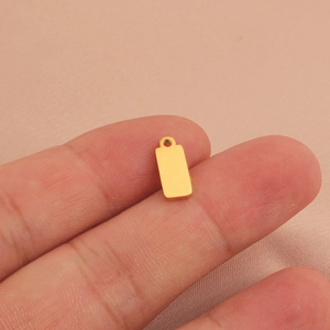 Polished gold stainless steel rectangular pendant held by fingers for size reference