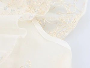 Détail de broderie de paillettes et motifs en fil d'or sur robe ivoire à volants