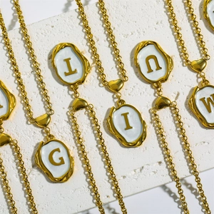 Macro shot of gold-plated capital letter pendants with white enamel on a white stone surface