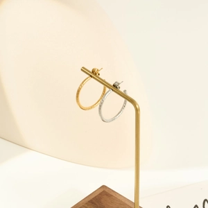 Detail of gold and silver textured hoop earrings on a metal jewelry display stand