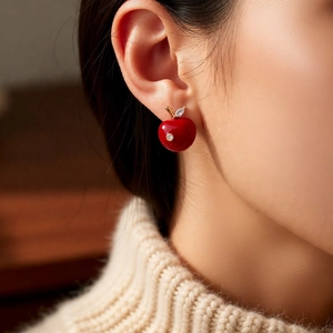 Detail of red apple stud earrings with marquise leaf on model with cozy knitwear