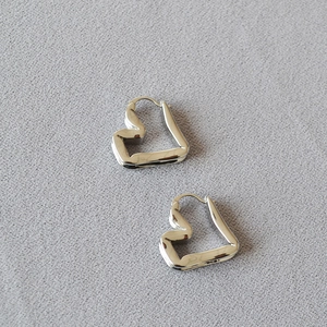 Close-up of silver folded heart earrings with a metallic finish on textured fabric