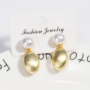 Macro detail of gold brushed metal drop earrings with white pearls on a display card