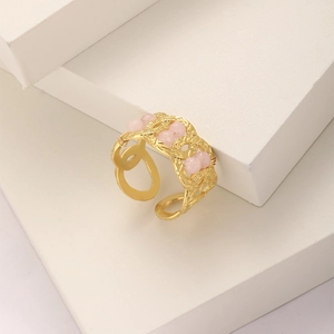 Detailed view of an open golden chain ring with pink beads on geometric blocks