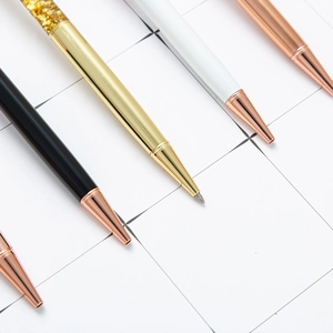 Chic metal ballpoint pens in black, gold, and rose gold with glitter decoration on white grid