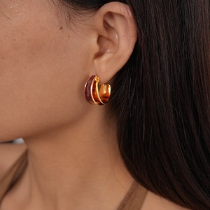 Close-up of 18k gold plated double C-shaped earrings with red-brown enamel on model
