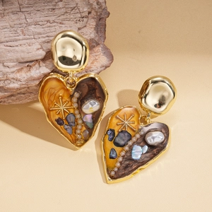 Macro shot of boho heart earrings with baroque pearls and blue shell pieces on wood