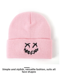Close-up of pink knitted beanie featuring a black stitched smiley face embroidery