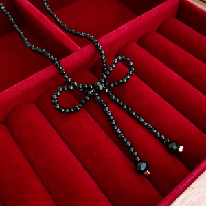 Close-up of black beaded bow necklace with faceted crystal details in red velvet box