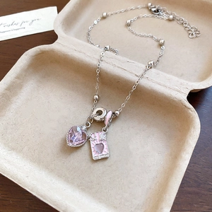 Macro shot of pink crystal heart and rectangular enamel pendant on silver chain