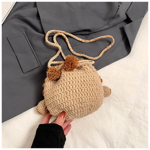 Detail of beige hand-knitted drawstring bag with brown pom poms and textured wool