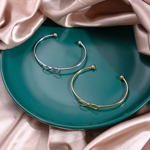 Detailed view of infinity knot open bangles in gold and silver finish on silk fabric