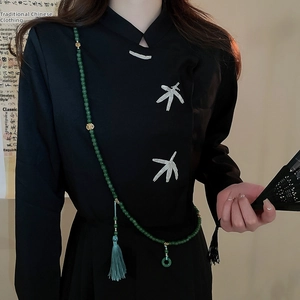 Détail de perles vertes avec pompon bleu clair et anneau de jade sur haut brodé noir