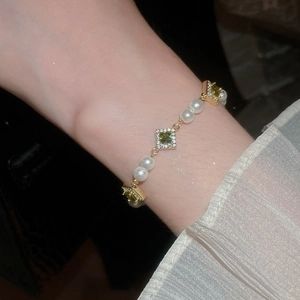 Detailed shot of gold bracelet with green zircons and white pearls on woman's wrist