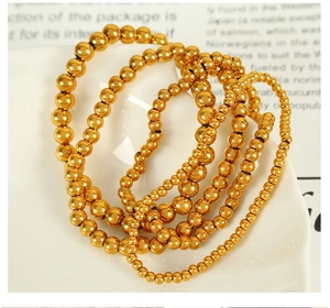 Detailed view of layered gold steel ball bracelets with various bead sizes on white ceramic