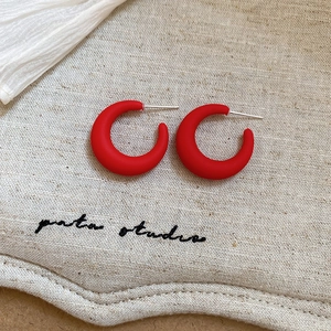 Detail of matte red C-shaped acrylic earrings with silver needles on a textured fabric