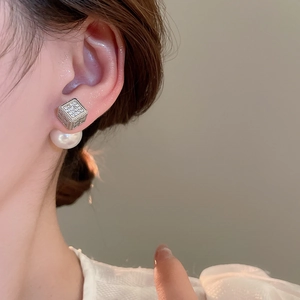Detailed close-up of a square zircon stud earring with a large pearl back on a model