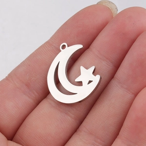 Hollow moon and star stainless steel pendant held on fingertip to show scale