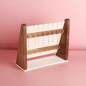 Walnut wood necklace display stand with gold hooks and cream velvet backing on pink background
