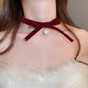 Close-up of a burgundy velvet bow choker with a white pearl drop on a female model